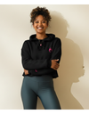 Woman wearing a black hoodie and teal shorts against a beige background
