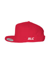 A red flat-brim snapback hat by Something Light Clothing. The front features a centered, white embroidered circular "SLC" monogram logo. An authentic "The Authentic Yupoong Snapback" silver sticker is visible on the top of the brim.