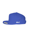 A royal blue flat-brim snapback hat by Something Light Clothing. The front features a centered, white embroidered circular "SLC" monogram logo. An authentic "The Authentic Yupoong Snapback" silver sticker is visible on the top of the brim.